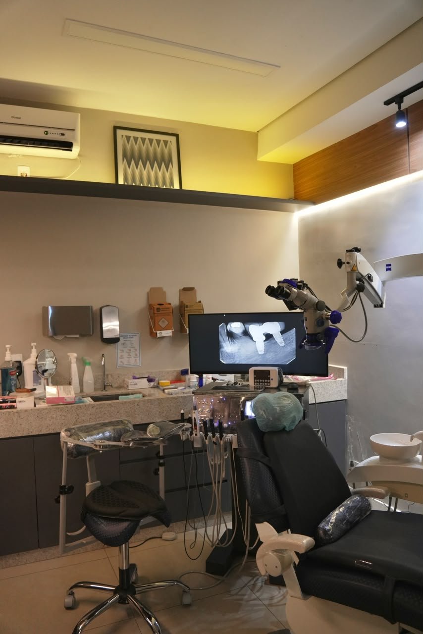 Sala clínica com cadeira odontológica e microscópio.
